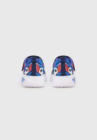 Siniset urheilukengät, joissa on jalkapalloa ja liekkikuviota, valkoinen pohja ja kangaspäällinen. Takakuvassa näkyy kaksi vetokahvaa.