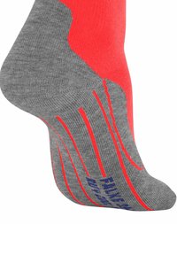 Szara i czerwona skarpetka sportowa z czerwonymi paskami i niebieskim napisem na podeszwie, zobaczona z boku z uniesionym piętą.