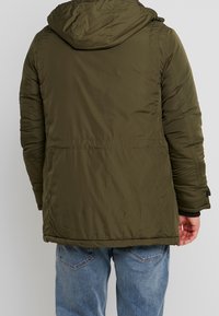 Olivgrön isolerad jacka med huva, texturerat tyg och elastiska ärmslut. Har en rak ryggdesign och en åtsittande midja.