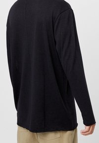 Czarna koszula z długim rękawem o luźnym kroju, okrągłym dekoltem, teksturowanej tkaninie i prostym obszyciu. Brak widocznych logo lub wzorów.