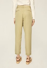 Pantaloni verde chiaro, morbidi e a vita alta con orli risvoltati. Tessuto liscio con tasche posteriori, abbinati a sandali con zeppa color marrone.