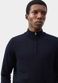 Granatowy sweter z wysokim kołnierzem i pół-zamkiem, wykonany z gładkiej dzianiny, charakteryzujący się minimalistycznym wzornictwem bez wzorów.