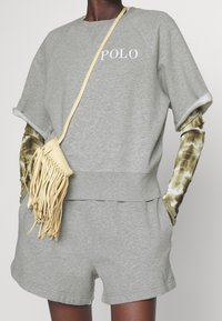 Šedá bavlněná mikina s bílým logem "POLO", kombinovaná s odpovídajícími šortkami. Součástí je žlutá kožená taška přes rameno s třásněmi.