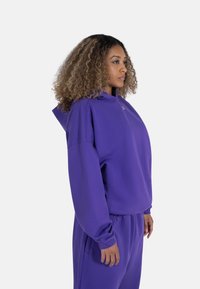Lilla hettegenser med høy hals og oversized design, med lange ermer og ribbede detaljer. Kombinert med matchende lilla bukser.