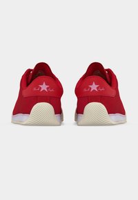 Ζευγάρι κόκκινων αθλητικών παπουτσιών χαμηλού προφίλ με λευκές σόλες, απεικονιζόμενα από πίσω, με ροζ αστέρι και το κείμενο «Chuck Taylor» στις ετικέτες της φτέρνας.