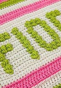 Gehaakte vloerkleed met groene en roze strepen en verhoogde groene tekst, gemaakt van gestructureerd garen, een mix van zachte en levendige kleuren.