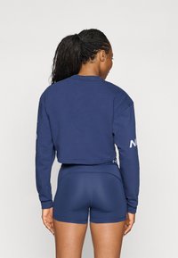 Felpa croppata blu navy con maniche lunghe, caratterizzata da un piccolo logo sulla manica destra, abbinata a pantaloni corti aderenti coordinati.
