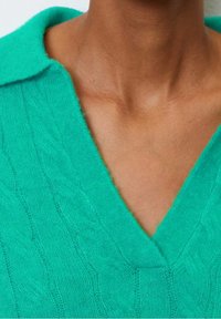 Green knitted sweater featuring a textured cable design, v-neckline, and a soft collar. Material appears lightweight and cozy.