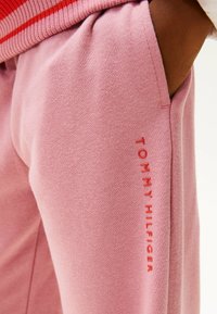 Roze joggingsbroek van zacht materiaal met een relaxte pasvorm. Kenmerkt zich door de rode "TOMMY HILFIGER" branding langs het linkerpijp en een elastische tailleband.