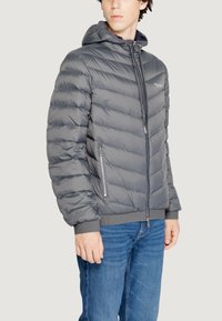Chaqueta acolchada gris con capucha, con cierre frontal con cremallera, puños elásticos y bolsillos laterales. Paneles texturizados con un acabado liso.
