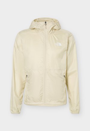 Lys beige hettejakke med full front glidelås, glidelåslommer på sidene, elastiske mansjetter og The North Face-logo på brystet.