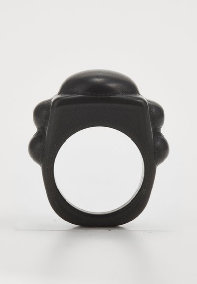 Black rubber ring with a rounded top and two bulbous side accents. Smooth texture and simple geometric shape, featuring a hollow center.