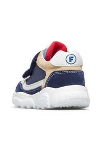 Dětské tenisky v námořnické modré, béžové a bílé barvě s červenou podšívkou, suchým zipem a texturovanou bílou podešví, zobrazené z pravého zadního úhlu.