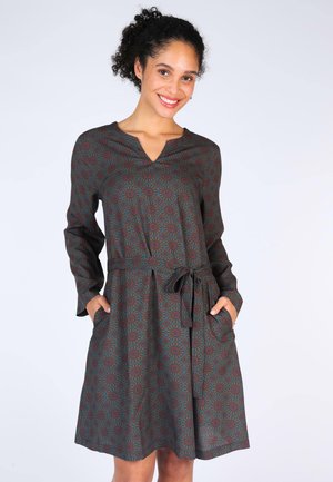 Langärmliges Kleid aus dunkelgrünem Stoff mit floralem Muster in Weinrot und Blau. Enthält einen V-Ausschnitt, einen Bindegürtel und seitliche Taschen.
