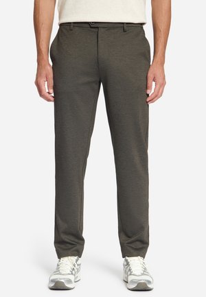Mann trägt dunkelgraue Slim-Fit-Hosen und weiße Sneakers, steht mit locker hängenden Armen neben dem Körper.