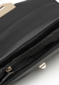 Interior de bolso de piel negra con compartimento con cremallera, accesorios en dorado y forro de textura suave. Cuenta con un cierre de broche seguro.