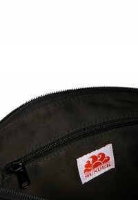 Bolsita de tela negra con cierre de cremallera, que cuenta con una etiqueta blanca con un diseño naranja y el texto "SUNDEK" en el interior.