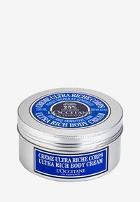 Silverfärgad, rund burk med blå etikett, som innehåller 200 ml kroppskräm, med text om sheasmör och hudtyp.