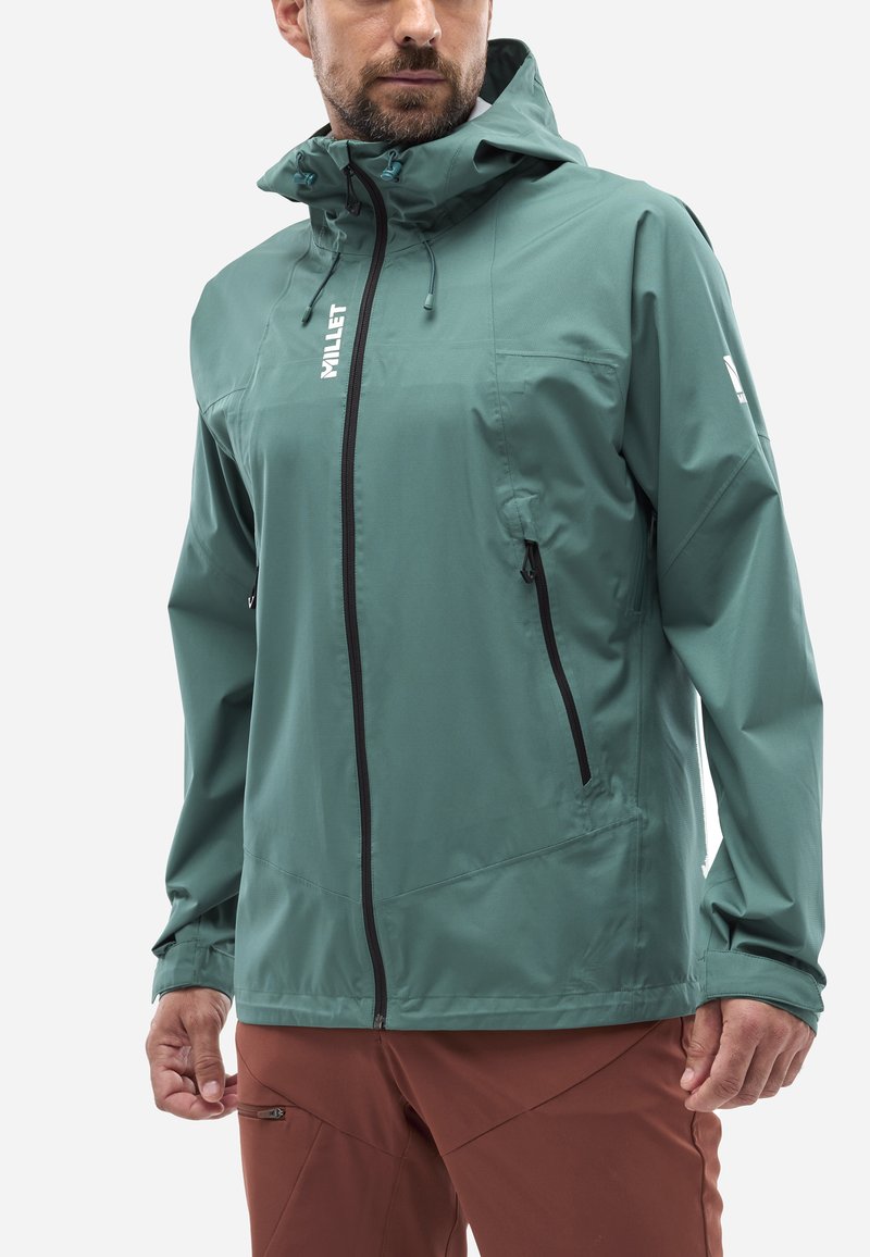 Veste pour homme en teinte teal, fabriquée dans un matériau léger. Elle dispose d'une capuche, d'une fermeture éclair sur le devant et de deux poches latérales zippées. Texture lisse avec des détails de logo.