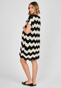 Abito a maglia zigzag bianco e nero con maniche corte, motivo testurizzato e orlo a scallop, abbinato a sandali neri a scivolo.