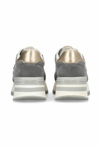Un paio di sneakers grigie e oro viste da dietro, con colletto imbottito e suole bianche spesse con strisce grigie chiare.