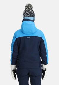 Marineblau und hellblaue Skijacke mit Kapuze, gerippten Bündchen und weißen Handschuhen. Verfügt über ein Logo und eine strukturierte Strickmütze mit Bommel.