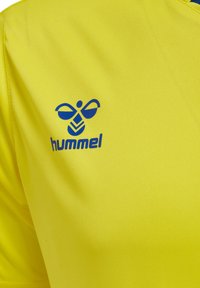 Gul sportströja i lättviktsmaterial med en blå logotyp av en bi och "hummel"-text på övre vänstra sidan.