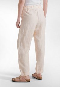 Lyserøde, brede hørbukser med elastisk talje og afslappet pasform, kombineret med brune sandaler med to stropper.