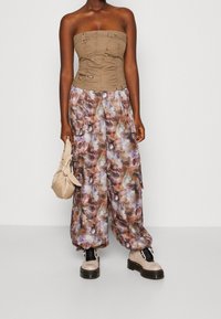 Beige strapless topp med veckad tyg och knappdekorationer, kombinerat med löst sittande, flerfärgade mönstrade cargobyxor och tjocka krämfärgade stövlar.