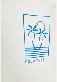 Maglietta bianca con una grafica blu raffigurante due palme, un sole e strisce orizzontali. Sotto il disegno è riportata la scritta "GOODTIMES".