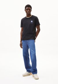 T-shirt nera a maniche corte con scollo rotondo e design stampato del sole. Indossata con jeans blu a gamba dritta e sneakers chiare.