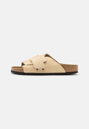Light beige leather slide sandal with dual adjustable straps. Natural cork footbed and textured rubber sole. Open toe design.