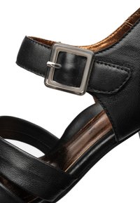 Sort damesandal i læder med firkantet sølvspænde og to frontremme, nærbillede af ankel og sidelayout.