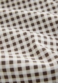 Tissu à motif vichy marron et blanc avec des plis doux et une surface légèrement texturée.