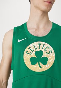 Homme portant un maillot de basketball vert des Boston Celtics avec logo de trèfle et swoosh Nike sur fond blanc.