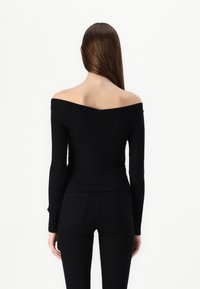 Svart av- skulder strikket topp med lange ermer, tettsittende design og ribbet tekstur, parret med svarte tettsittende bukser.