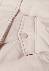 Gaiši rozā pufīgā jaka ar apļa pogu, diognālā kvadrātveida auduma faktūra un izšuvumi uz auduma.