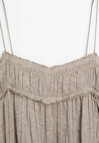 Débardeur marron clair plissé avec fines bretelles, corsage froncé et ourlet effiloché, confectionné dans un tissu texturé.