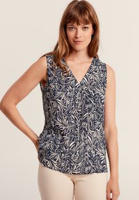 Top senza maniche blu navy con scollatura a V; presenta un motivo astratto di foglie bianche su tutta la superficie; tessuto morbido, vestibilità rilassata e orlo leggermente curvato.