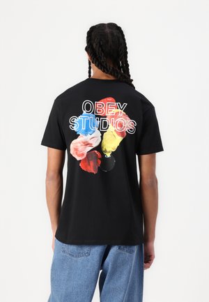Tricou din bumbac negru cu un grafic colorat de stropi de vopsea pe spate și „OBEY STUDIOS” scris cu litere albe deasupra. Croit lejer.