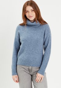 Light blue, soft knit sweater with a high, rolled turtleneck, long sleeves, and ribbed cuffs and hem. Worn with gray pants.