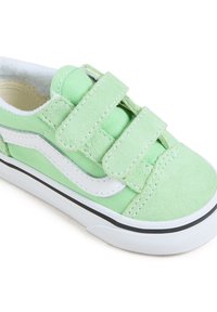 Roheline sametist sneaker, millel on valged kangast aktsendid, topelt Velcro rihmad, tekstureeritud pind ja kummist põhja mustad detailid.