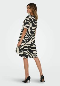 Robe noire et crème à imprimé zèbre avec des manches courtes, jupe évasée et coupe décontractée, associée à des escarpins noirs.