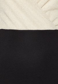Pull en tricot avec une section supérieure crème légèrement brillante et une section inférieure noire uni ; texture douce et design côtelé en bas.