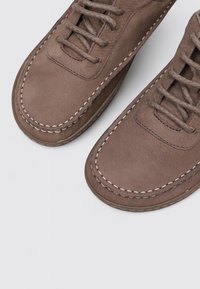 Chaussures en cuir marron avec une finition lisse, bout rond et détail de couture contrasté, comportant un système de laçage et une semelle flexible.