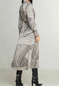 Vestito lungo con bottoni, caratterizzato da un motivo geometrico a strisce nere e beige, con maniche lunghe e vita aderente, abbinato a stivali neri al ginocchio.