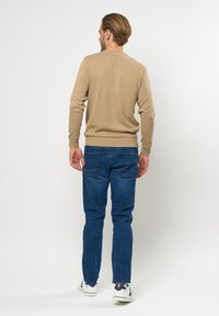Beige gebreide trui met lange mouwen, ronde hals en geribbelde manchetten, gecombineerd met donkerblauwe jeans en witte sneakers. Achteraanzicht weergegeven.