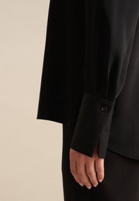 Czarna koszula z długim rękawem, z mankietami na guziki, gładką teksturą, dopasowanym fasonem i bocznymi rozcięciami dla swobody ruchów.