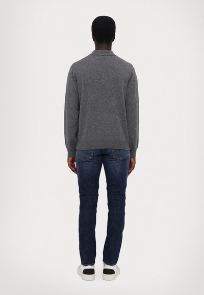 Grauer Strickpullover mit langen Ärmeln und geripptem Saum, kombiniert mit dunkelblauen Jeans und weißen Sneakers mit schwarzen Akzenten.