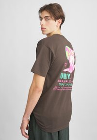 Brun bomulds t-shirt, rund hals, korte ærmer, med farverigt grafik på ryggen med tekst i pink og turkis. Afslappet pasform.